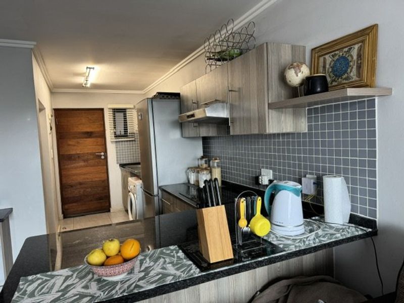 A functional kitchen featuring granite countertops, modern laminate cabinetry, a tiled backsplash, and an integrated extractor fan.