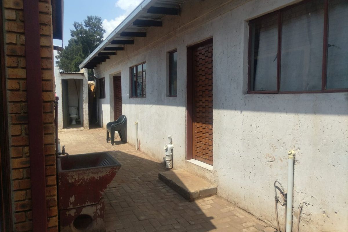 Rear exterior view of the property featuring brick paving, a concrete wash trough, and access doors along the side of the building.