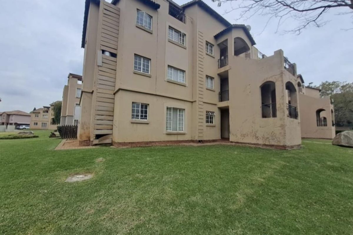 Exterior view of a multi-story residential building featuring plastered walls, balconies, and tiled roofing, set within a communal garden area.