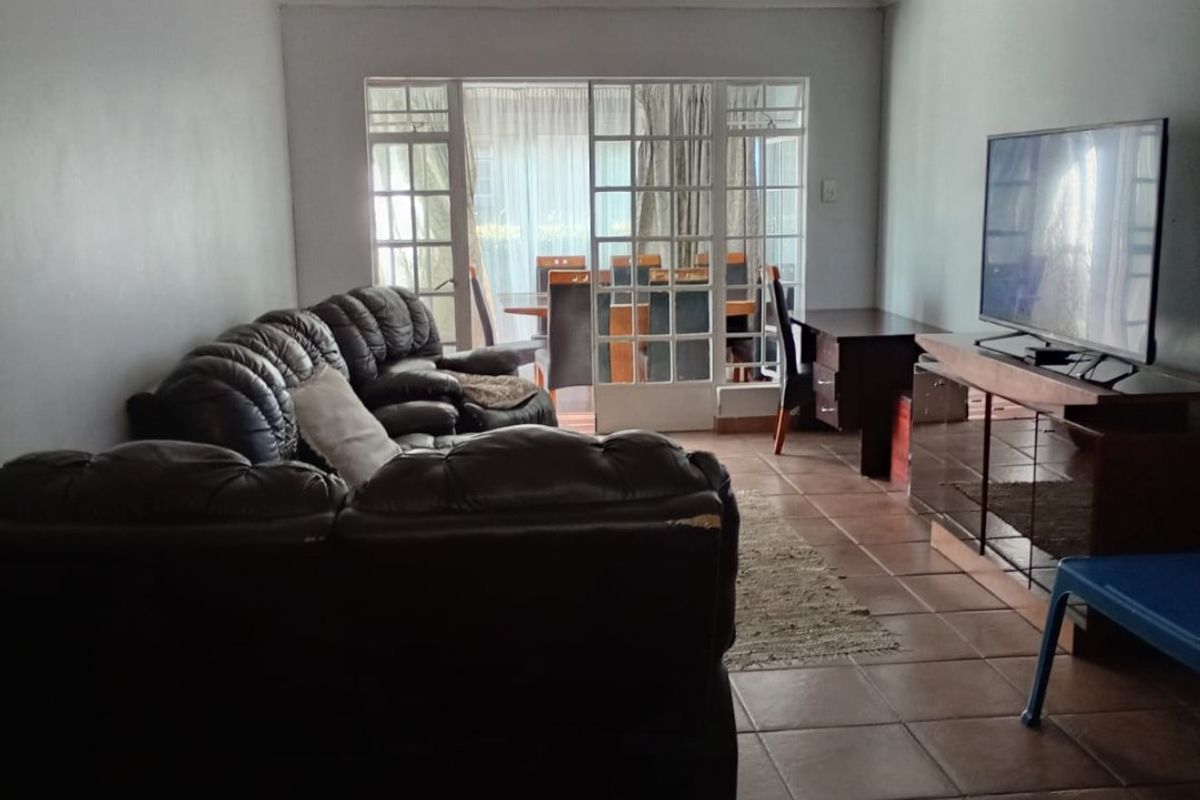 A living room featuring tiled flooring and glass-paned french doors leading to an adjacent dining area.