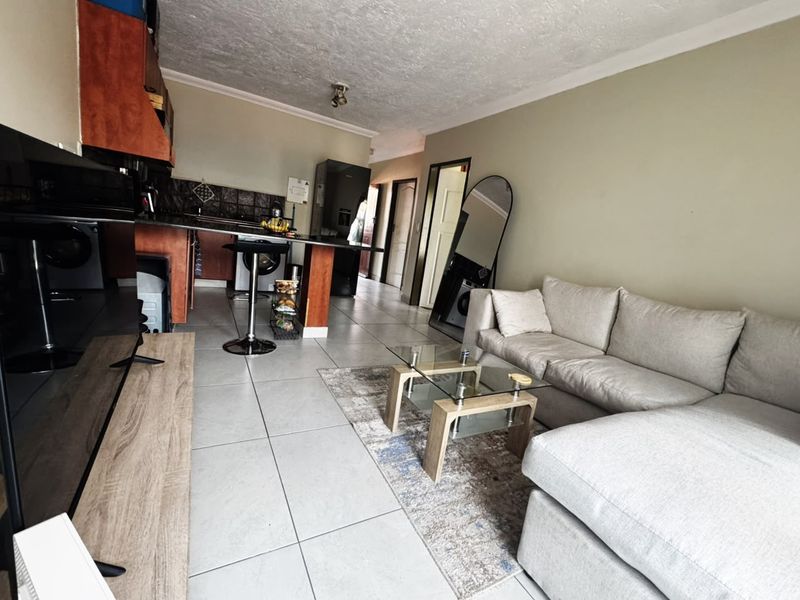 Open-plan living area featuring tiled flooring, a functional kitchen with breakfast counter, and neutral wall tones, creating a versatile and connected living space.
