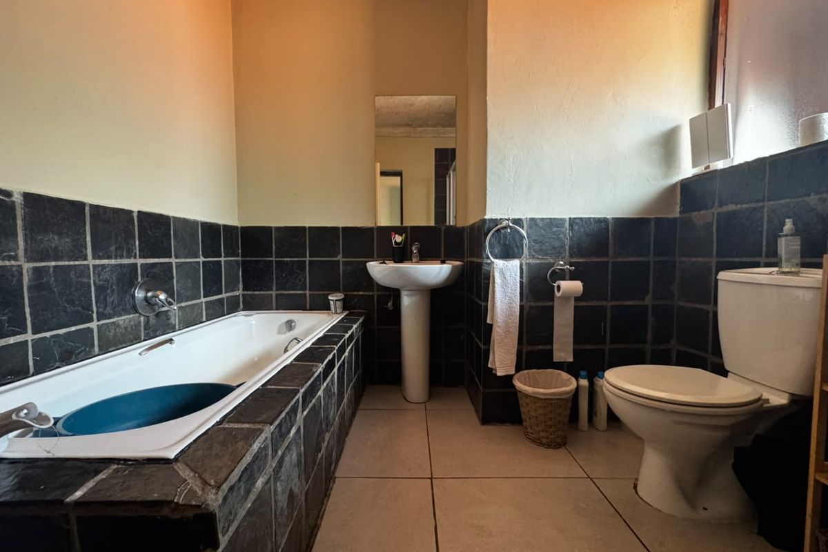 A functional bathroom featuring a built-in bathtub, pedestal basin, and toilet with dark tiled wall accents and neutral floor tiling.