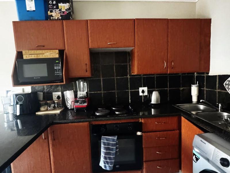 A functional kitchen featuring wooden cabinetry, black granite countertops, a tiled backsplash, and integrated oven and hob.