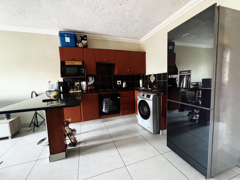 A functional kitchen featuring dark wood cabinetry, black granite countertops, tiled backsplash, and integrated appliances with neutral floor tiling.