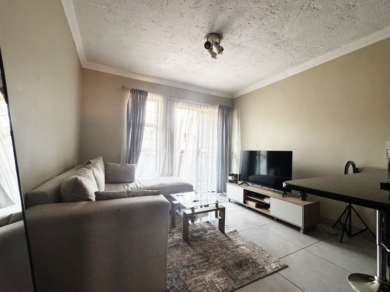 A comfortable living room featuring tiled flooring, a coved ceiling, and a sliding glass door that provides natural light.