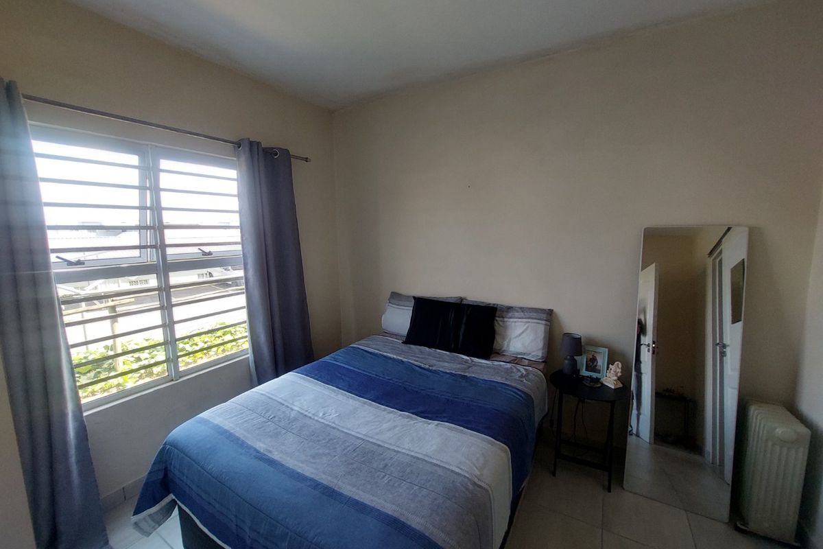 A functional bedroom featuring tiled flooring and a window fitted with security bars, providing natural light and ventilation.