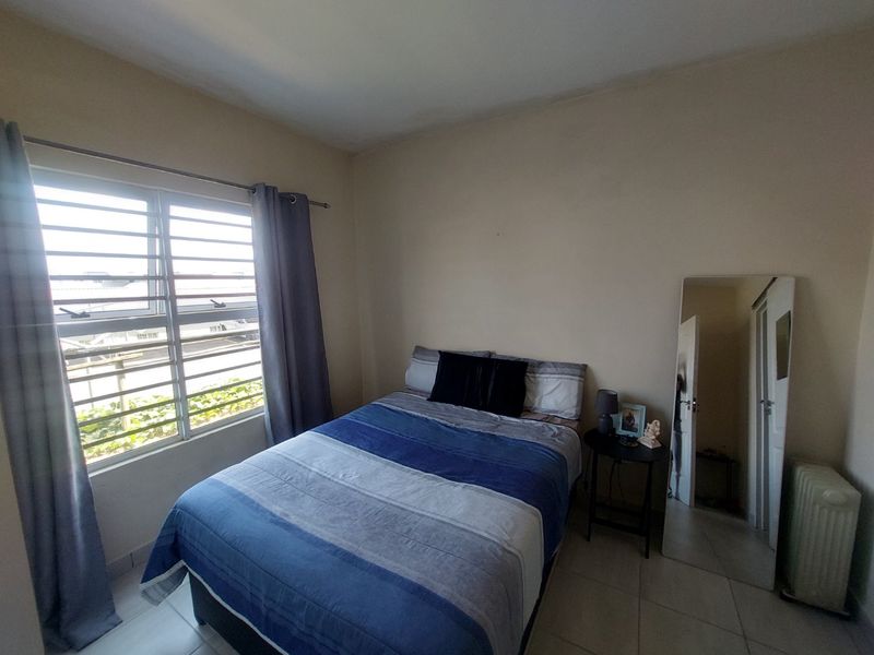 A functional bedroom featuring tiled flooring and a window fitted with security bars, providing natural light and ventilation.