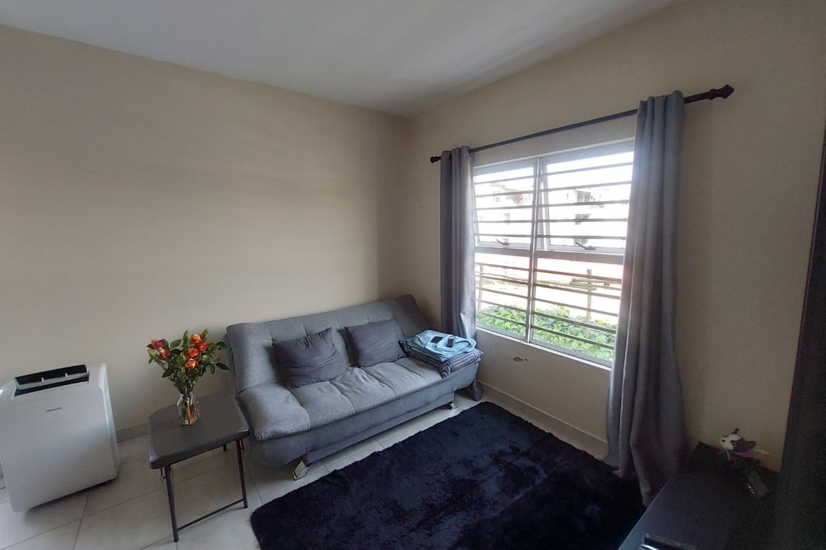 A compact living room featuring tiled flooring and a window fitted with security bars, providing natural light and a functional layout.