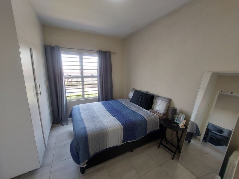 A functional bedroom featuring built-in cupboards, tiled flooring, and louvre windows, providing a clean and practical living space.