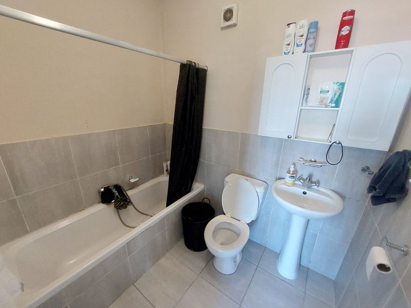 A functional bathroom featuring a bathtub with shower attachment, pedestal basin, toilet, and wall-mounted storage cabinet with neutral tiled finishes.