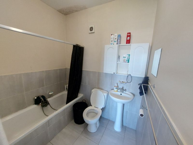 A functional bathroom featuring a bathtub, pedestal sink, toilet, and wall-mounted storage cabinet, with visible water staining on the ceiling requiring attention.