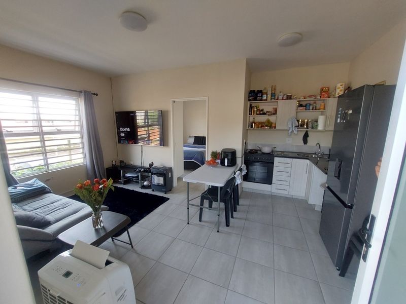 Open-plan living area featuring a functional kitchen with built-in cabinetry, tiled flooring, and a bright, connected lounge space.