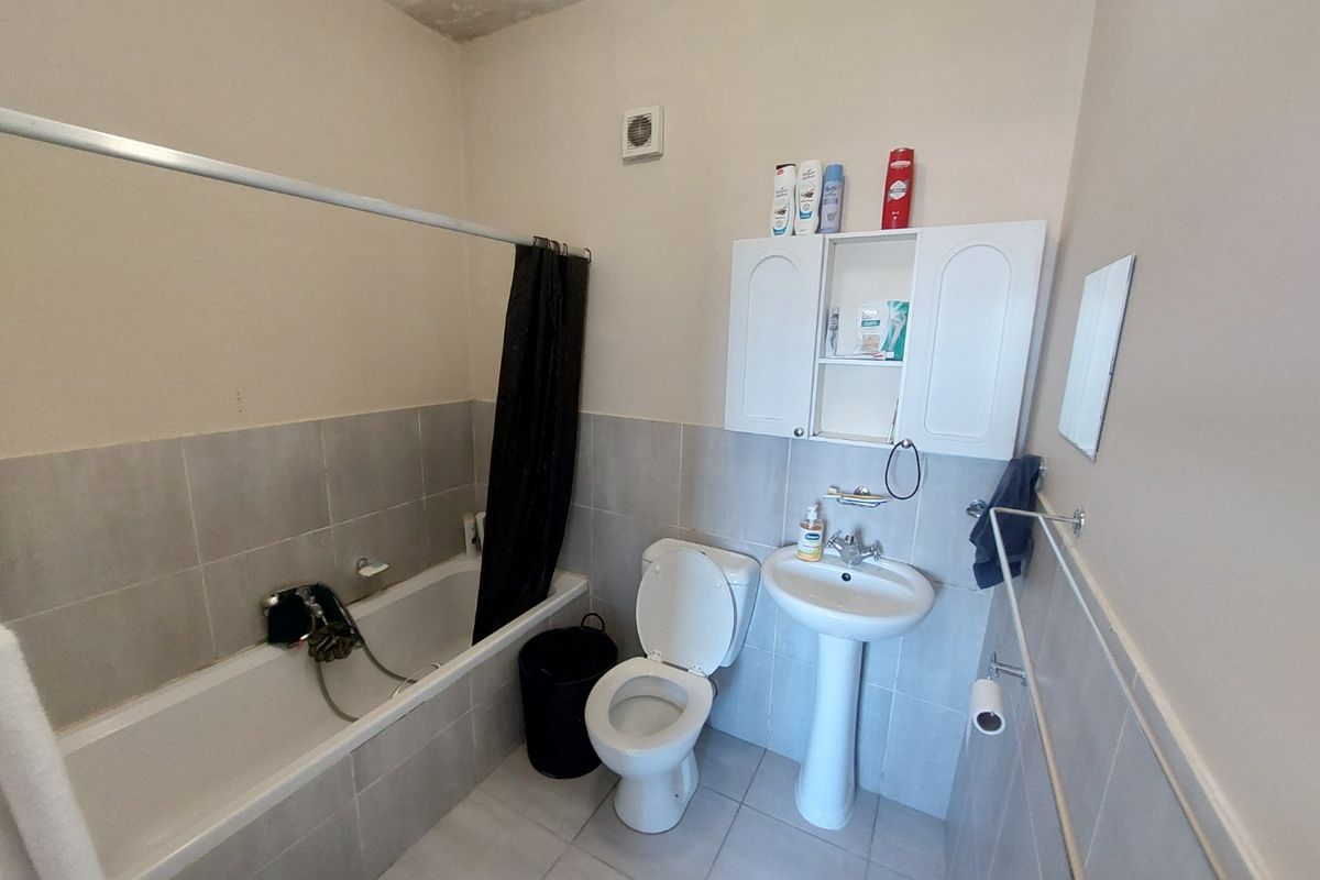 A functional bathroom featuring a bathtub, pedestal sink, and toilet, with tiled finishes and a wall-mounted storage cabinet.