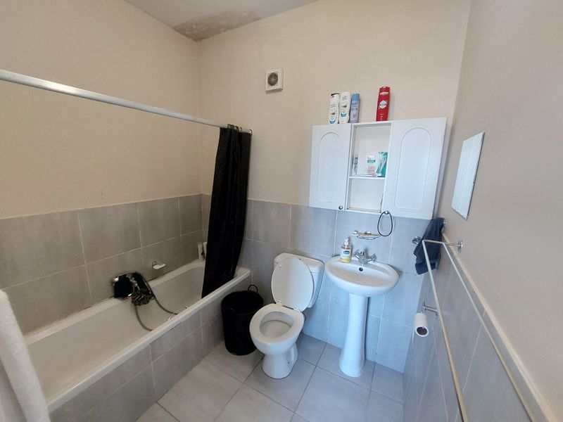 A functional bathroom featuring a bathtub, pedestal sink, and toilet, with tiled finishes and a wall-mounted storage cabinet.