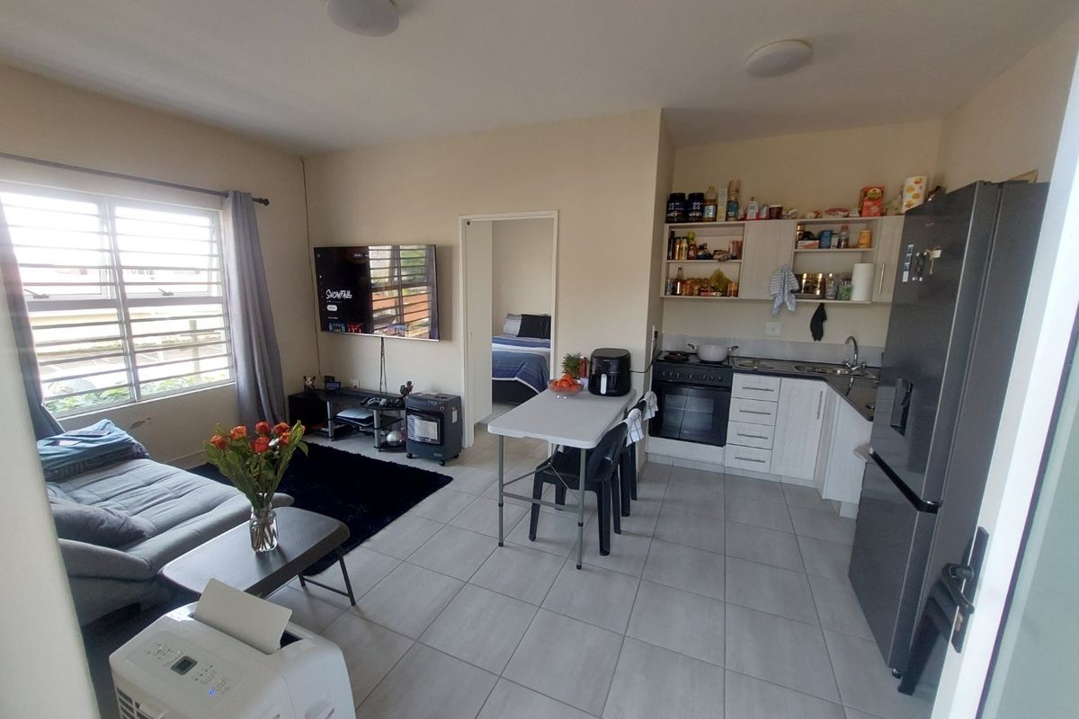 An open-plan living and kitchen area featuring tiled floors, functional cabinetry, and a built-in oven, providing a practical and versatile living space.