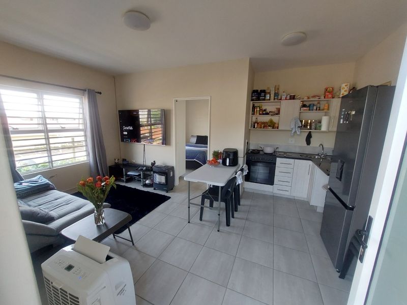An open-plan living and kitchen area featuring tiled floors, functional cabinetry, and a built-in oven, providing a practical and versatile living space.