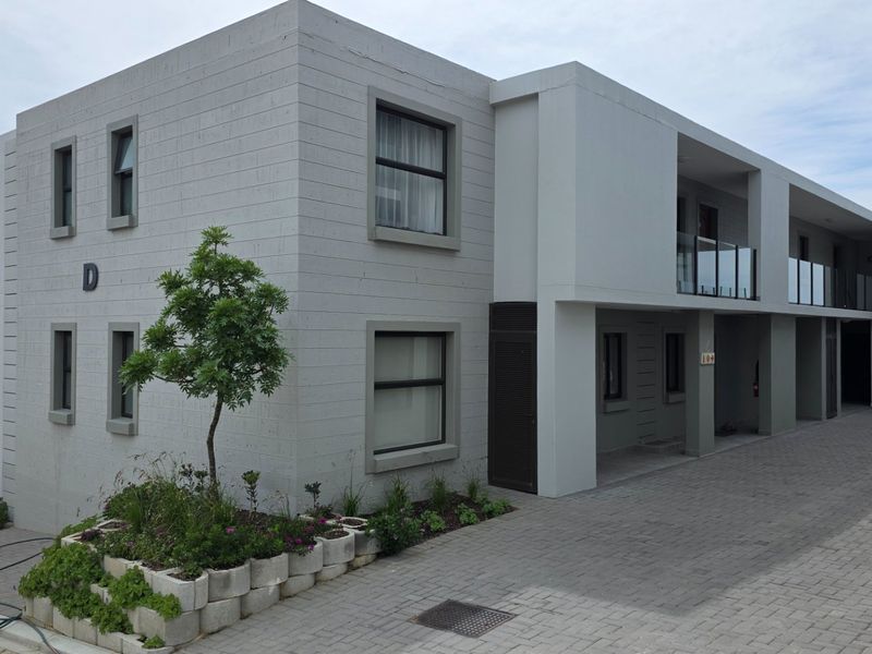 Modern apartment building exterior featuring a clean concrete block facade, paved driveway, and glass-railed balconies.