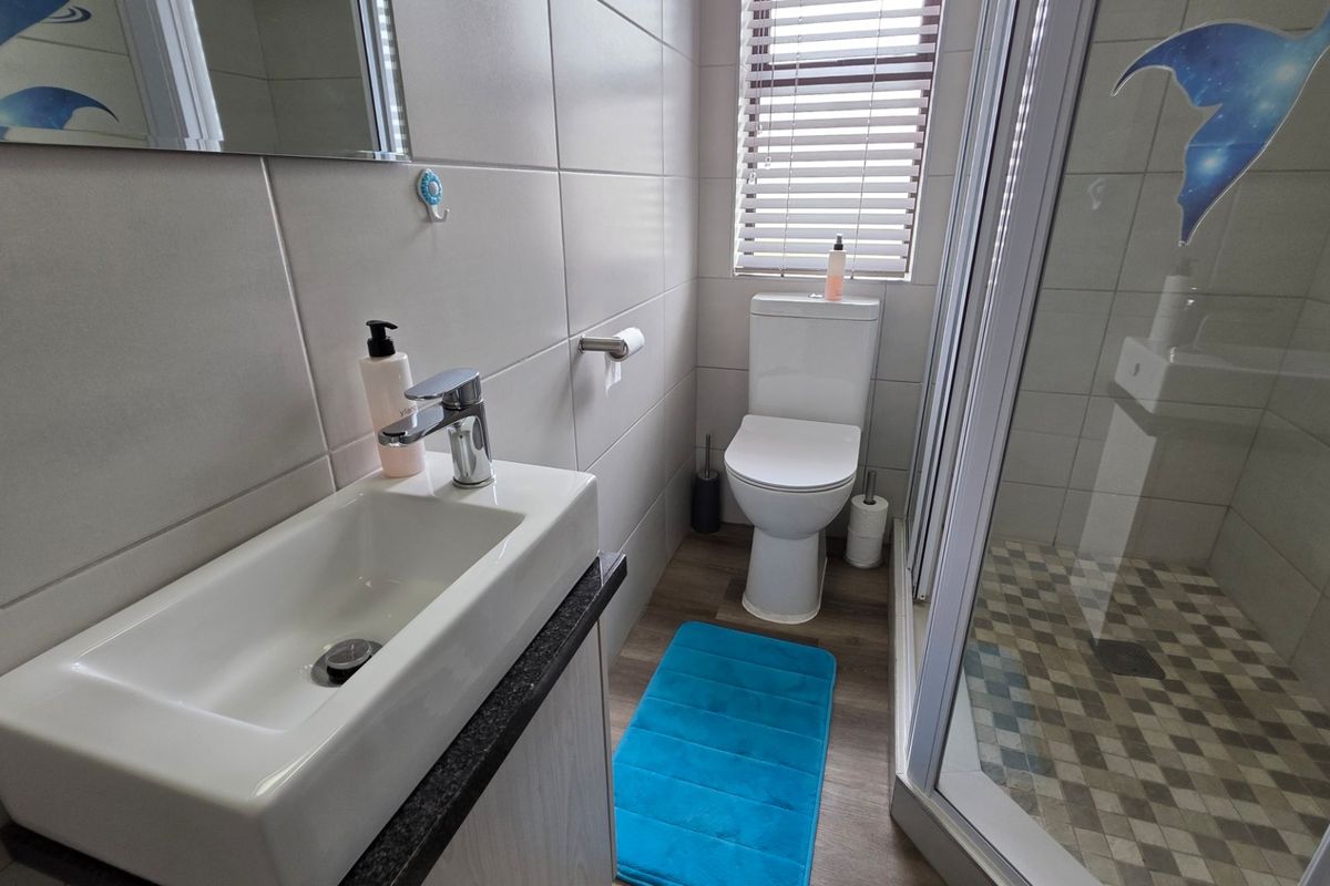 A modern, well-maintained bathroom featuring a vanity basin, toilet, and a glass-enclosed shower with tiled walls and laminate flooring.