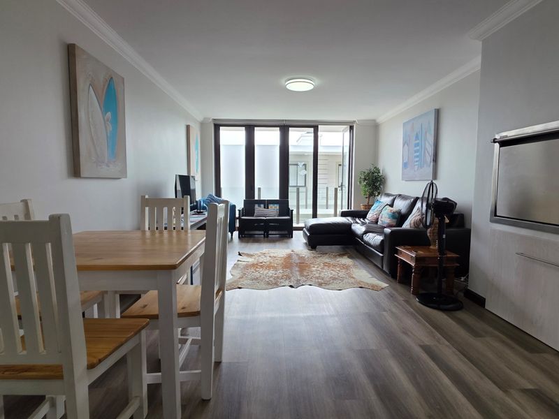 Open-plan living and dining area featuring modern laminate flooring, a built-in braai, and large sliding doors leading to an outdoor space.