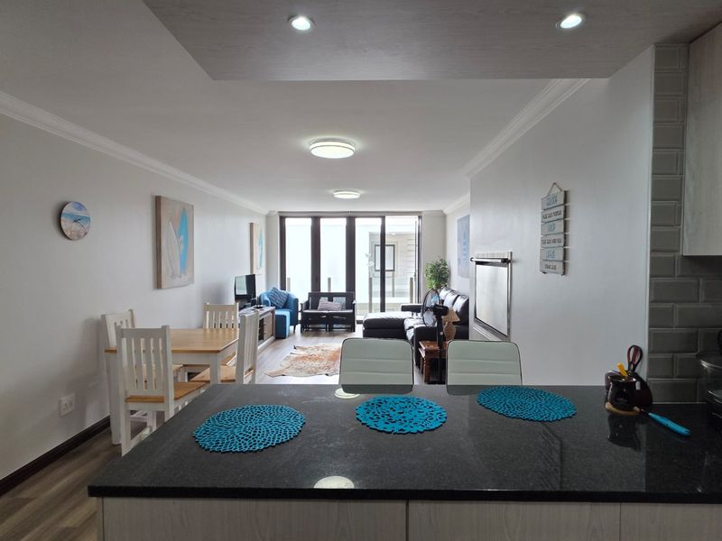 Spacious open-plan living area featuring a modern kitchen with granite countertops, subway tile backsplash, and seamless flow to the balcony through sliding glass doors.