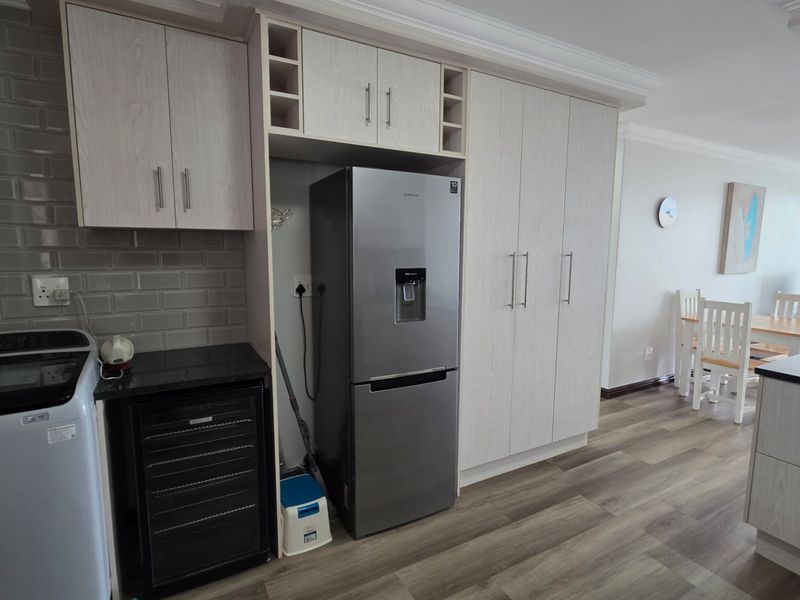 Modern open-plan kitchen area featuring light wood-grain cabinetry, subway tile backsplash, and dark granite countertops, seamlessly flowing into the dining and living space.