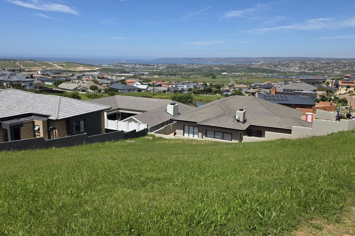 A wide-angle view overlooking a residential neighborhood and distant coastal landscape from a sloped vacant residential plot.