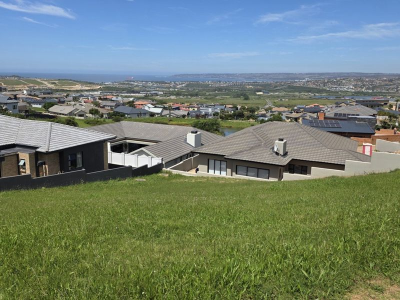 A wide-angle view overlooking a residential neighborhood and distant coastal landscape from a sloped vacant residential plot.