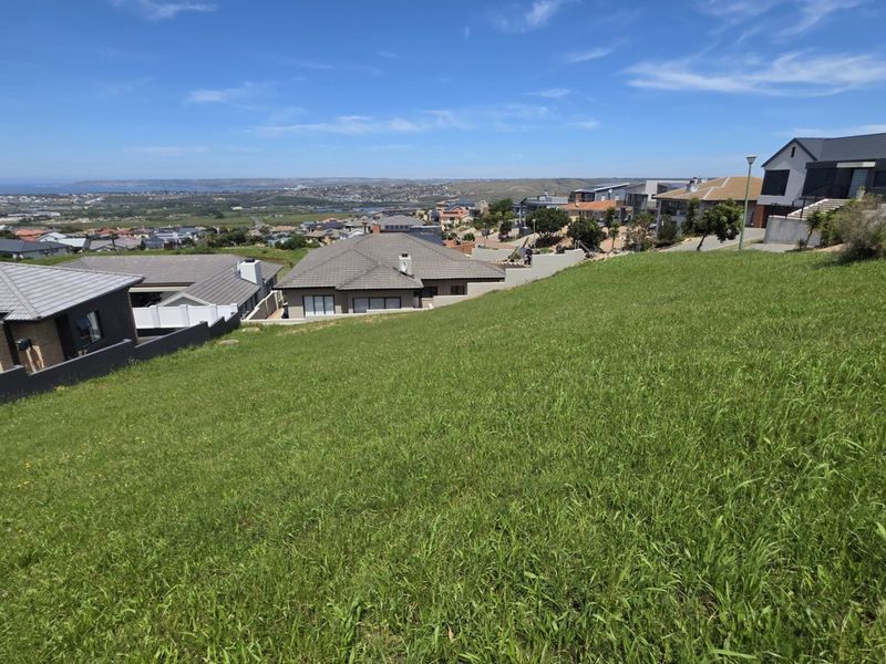 A view from a sloped residential vacant land plot overlooking the surrounding neighborhood and distant coastal landscape.