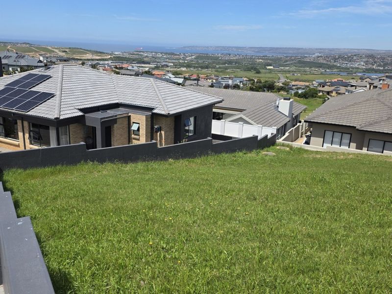 Elevated view overlooking a residential neighborhood and distant coastline from a vacant residential plot with established retaining walls.