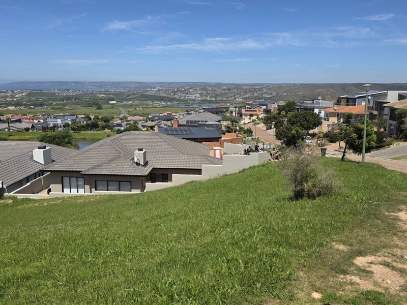 Elevated view overlooking a residential neighborhood and distant coastal landscape from a sloped vacant residential plot.