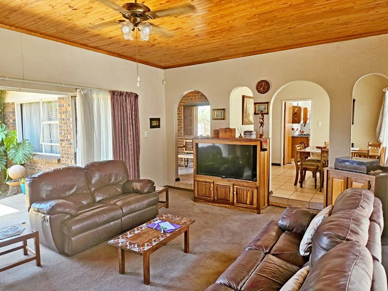 Spacious living room featuring a warm timber ceiling, ceiling fan, and classic arched doorways leading to the dining area and kitchen.