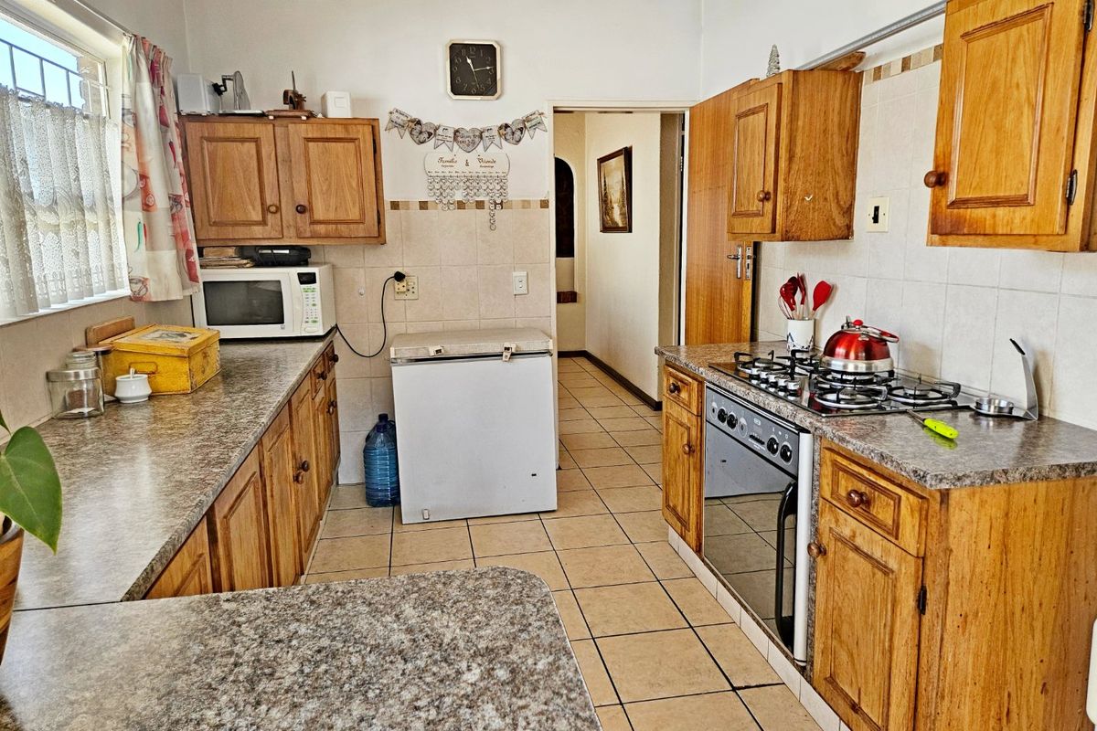 A functional kitchen featuring traditional wooden cabinetry, laminate countertops, a gas hob, and an integrated oven with tiled flooring and backsplash.