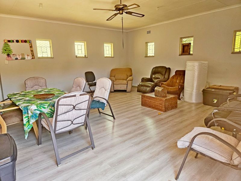 Spacious living area featuring light-toned laminate flooring, a ceiling fan, and multiple small windows providing natural light.