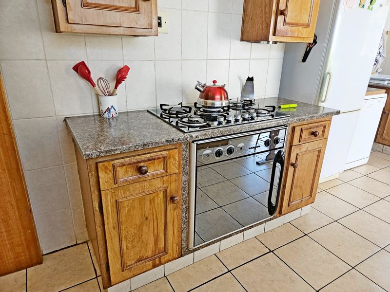 A functional kitchen area featuring wooden cabinetry, granite countertops, a built-in gas cooktop, and an oven, finished with ceramic wall and floor tiles.