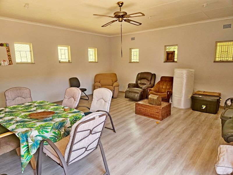 Spacious living area featuring light-toned laminate flooring, a ceiling fan, and multiple windows providing natural light.