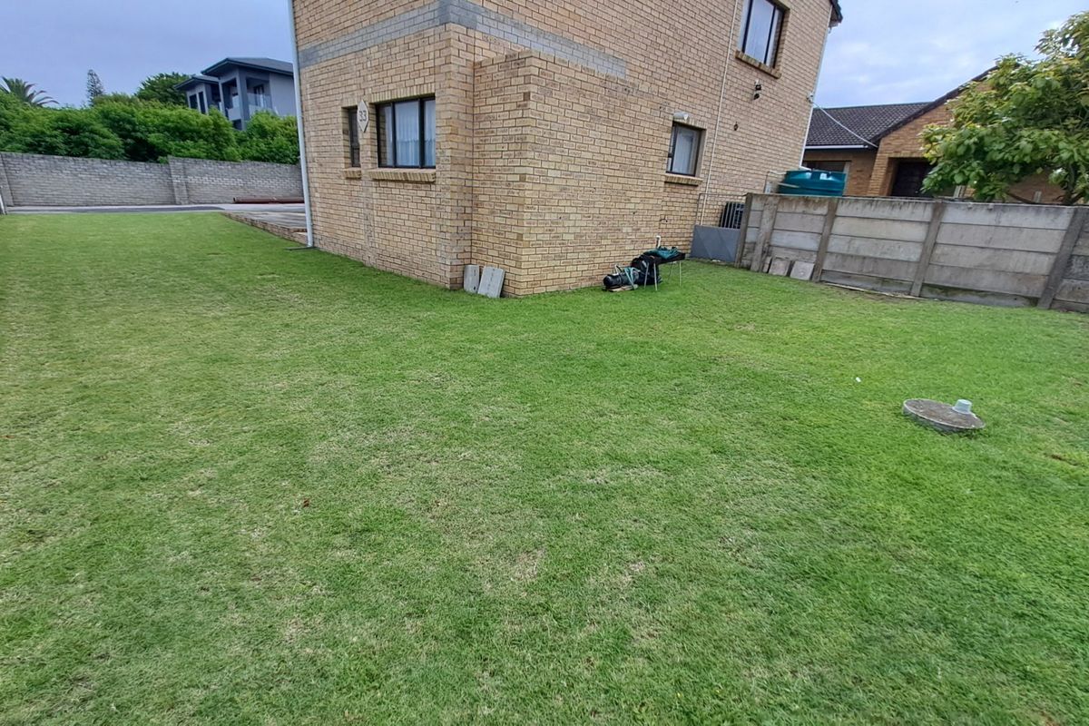 A spacious rear garden area featuring a well-maintained lawn, enclosed by precast concrete boundary walls and adjacent to the brick exterior of the property.