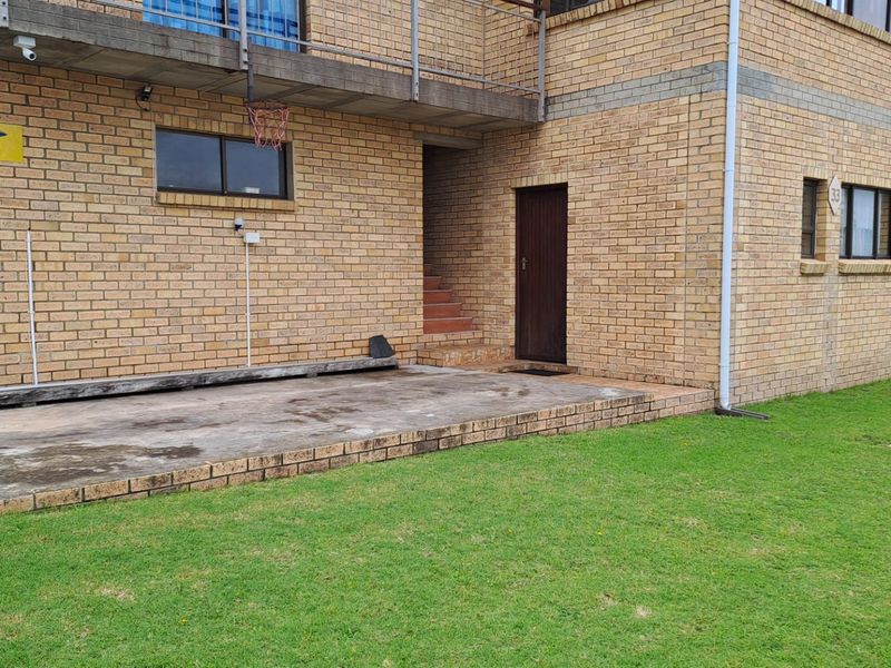 Rear view of the apartment building featuring a face brick facade, a concrete patio area, and an elevated balcony with metal railings.
