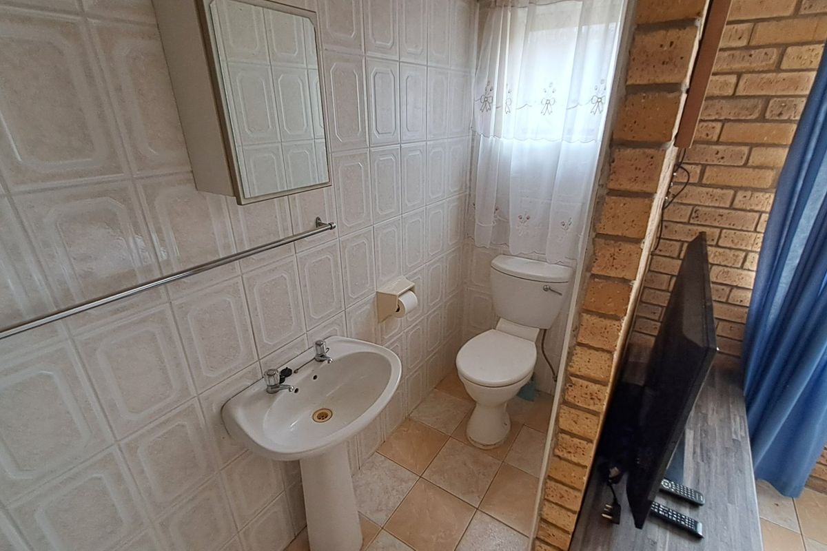 A functional bathroom featuring a pedestal basin, toilet, and tiled finishes, complemented by an exposed brick feature wall.