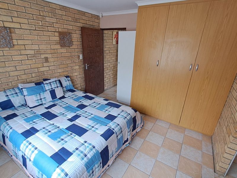 Bedroom featuring exposed brick walls, tiled flooring, and built-in wooden cupboards.