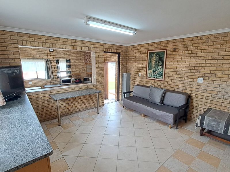 Open-plan living area featuring exposed brick walls, tiled flooring, and a convenient breakfast bar pass-through connecting to the kitchen space.