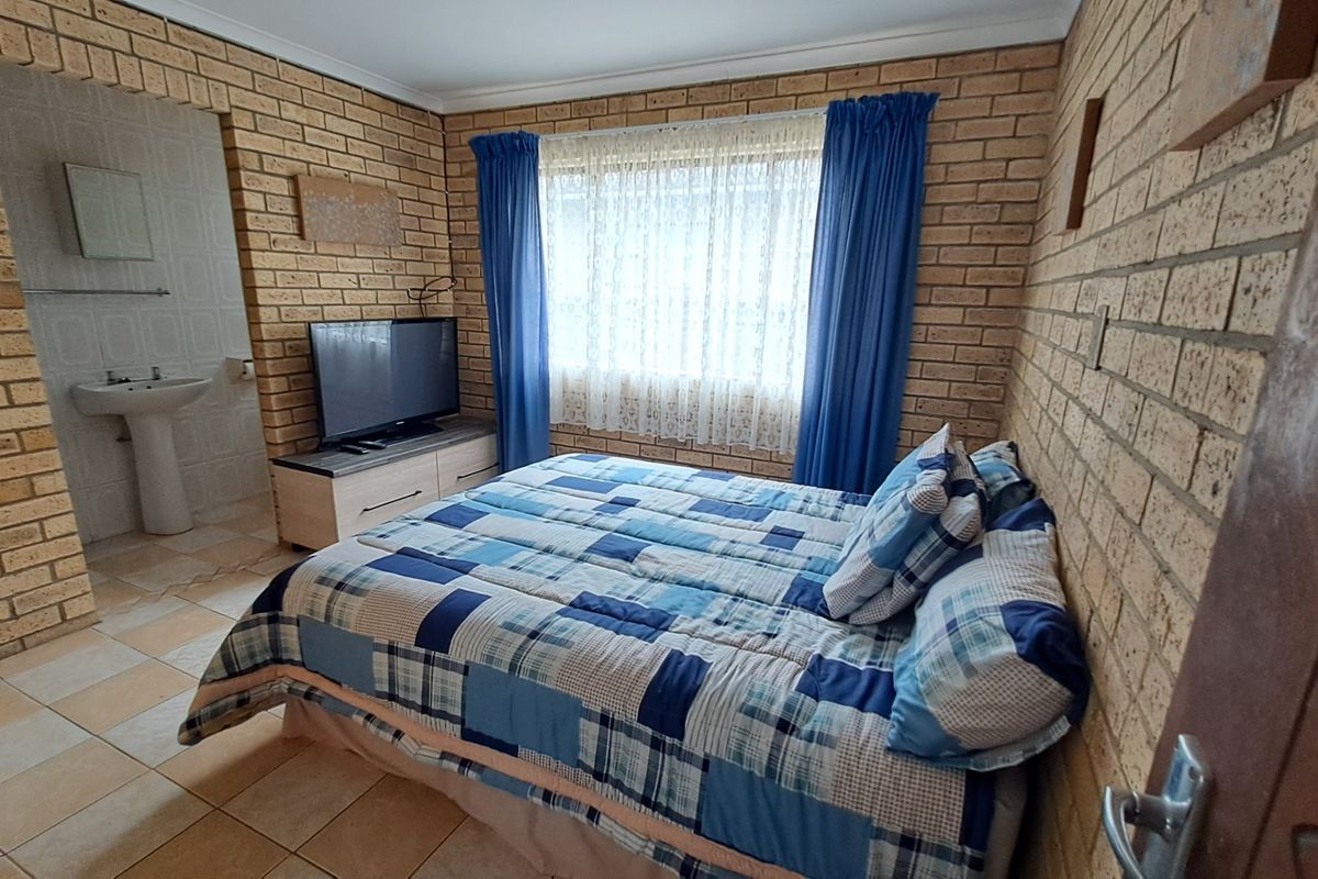 A bedroom featuring exposed brick walls and tiled flooring, with an integrated open-plan pedestal basin area.