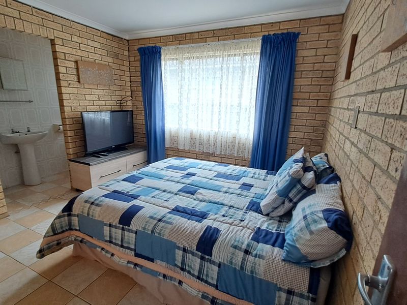 A bedroom featuring exposed brick walls and tiled flooring, with an integrated open-plan pedestal basin area.
