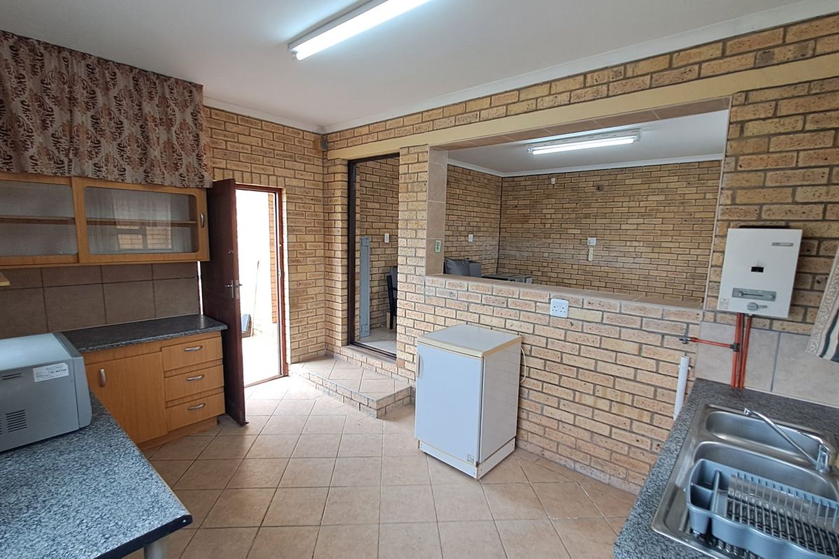 A functional kitchen featuring exposed brick walls, tiled flooring, built-in cabinetry, and a double bowl stainless steel sink with a wall-mounted gas geyser.