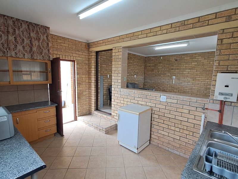 A functional kitchen featuring exposed brick walls, tiled flooring, built-in cabinetry, and a double bowl stainless steel sink with a wall-mounted gas geyser.