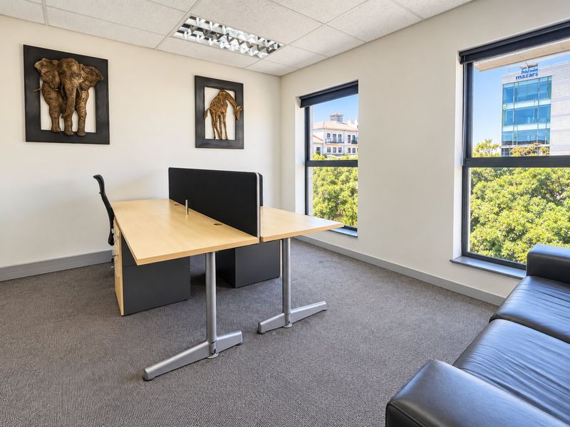 A bright and professional office space featuring carpeted flooring, recessed lighting, and large windows providing natural light and views of the surrounding area.