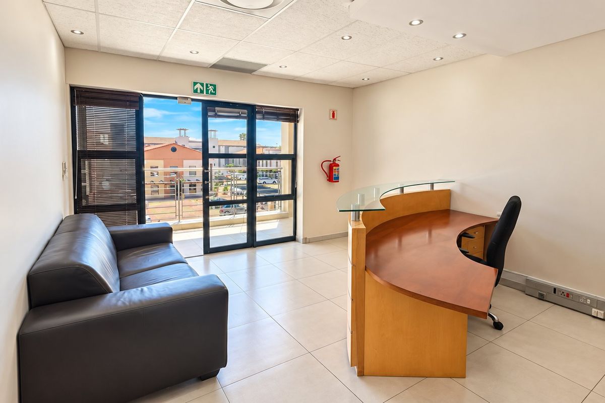 A bright, professional office space featuring tiled flooring, a suspended ceiling with recessed lighting, and direct access to a private balcony.