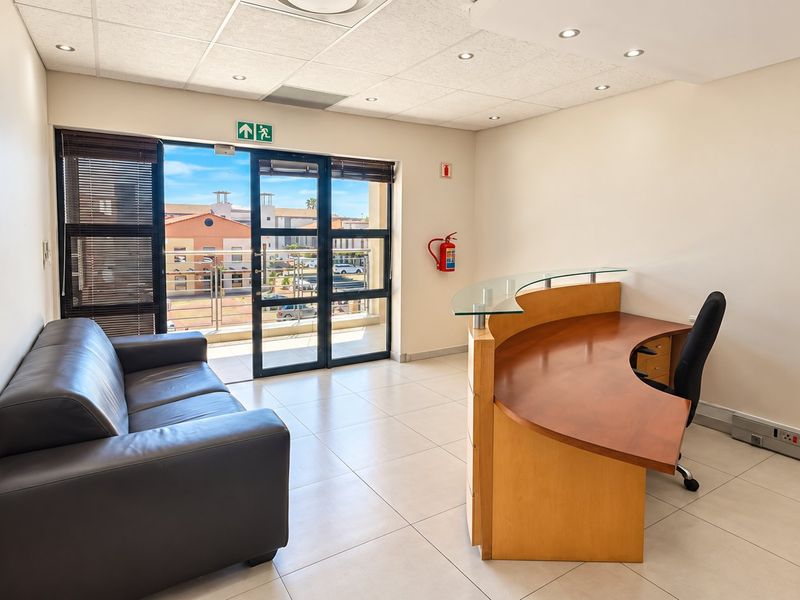 A bright, professional office space featuring tiled flooring, a suspended ceiling with recessed lighting, and direct access to a private balcony.
