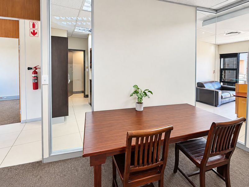 A modern commercial office space featuring glass partition walls, neutral finishes, and a combination of tiled and carpeted flooring.