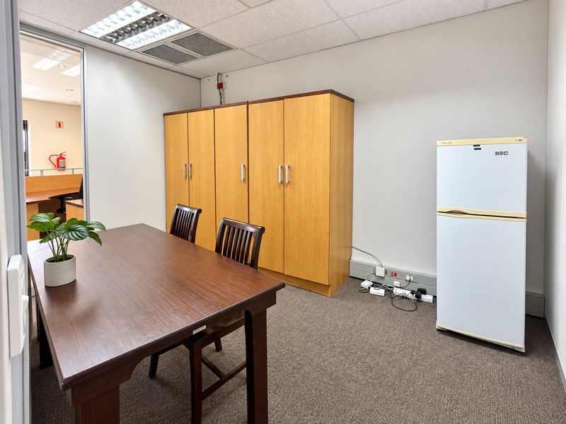 A functional office space featuring built-in wooden cabinetry, carpeted flooring, and a suspended ceiling with integrated lighting.