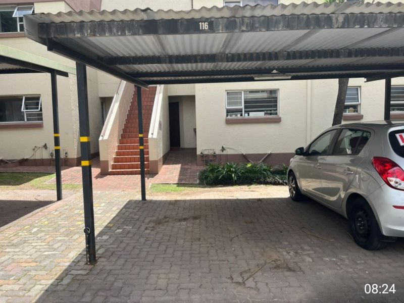 A covered carport parking space with paved driveway and access to an external staircase leading to the townhouse entrance.